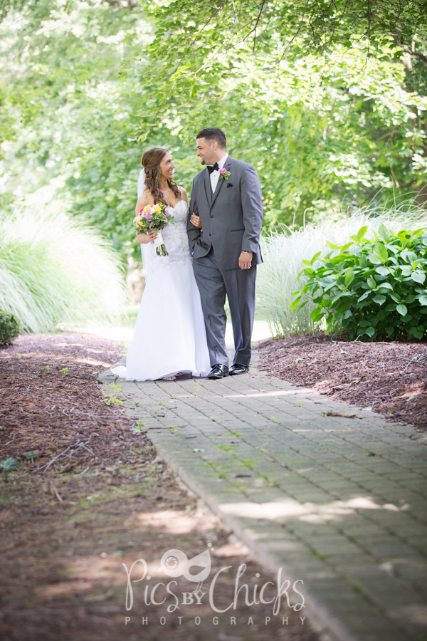 wedding photo of bride and groom walking on a path surrounded by trees.  Summer wedding photo
